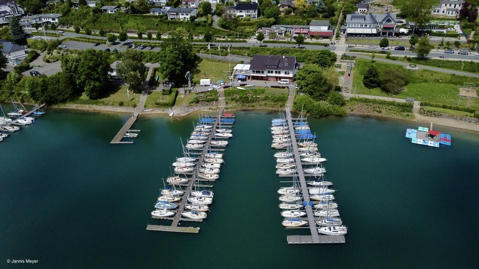 KSCH Luftaufnahme eines Yachthafens mit mehreren Booten und einem Steg, umgeben von grüner Landschaft und Wohngebieten.